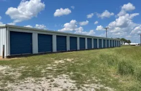 Outdoor storage units with blue roll up doors on grass with the sky and clouds in the background