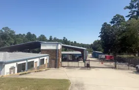Gated entrance to facility with covered parking and drive-up storage units behind it and the office building to the left