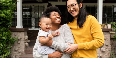 family holding baby standing outside of a home