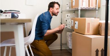 man wearing blue and brown crouching on the floor taking notes about storage boxes