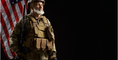 older soldier stnading with back to usa flag with a black background