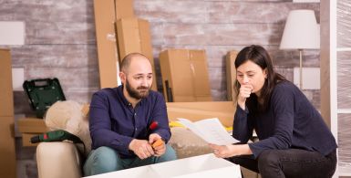 man and woman sitting on a couch reading papers with storage boxes behind them