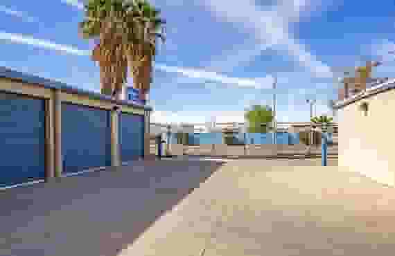 A row of exterior drive-up storage units. The fence is visible behind the units, as well as a StaxUP Storage sign.