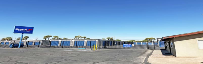 The front of the property. A StaxUP Storage sign stands beneath a blue sky. Behind a fence is a row of drive-up storage units.