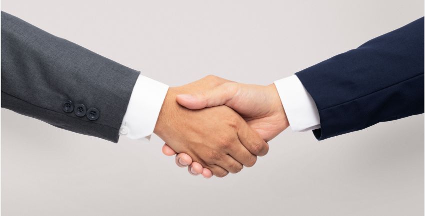 two people in suits with a white undershirt shaking hands on a gray background