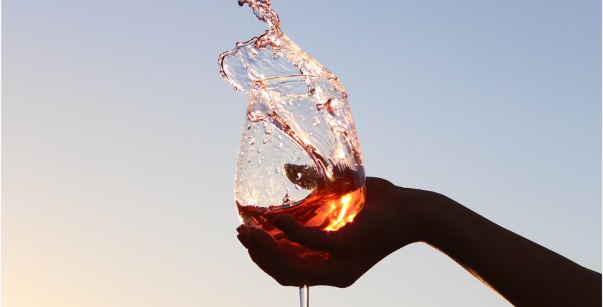 silhouette of a hand splashing a glass of wine on a background with a soft sunset