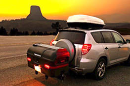 Stowaway cargo carrier on gray SUV driving through the canyon in sunset