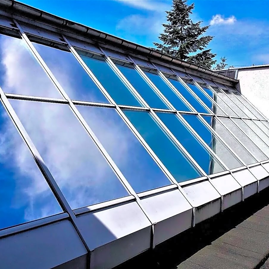 Reflekterende vinduesfolie på et skråt glastag, der spejler den blå himmel og skyer