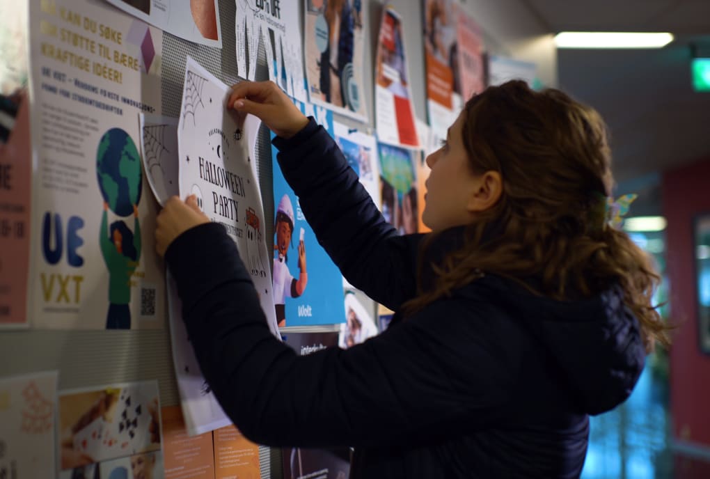 Student henger opp plakat på tavle