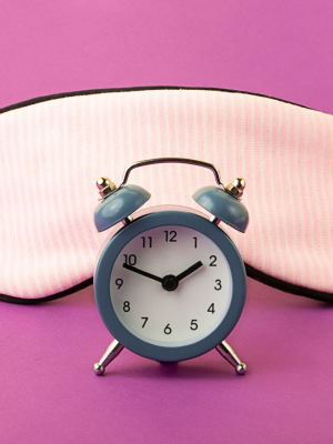 A blue alarm clock and pink eye mask on pink background