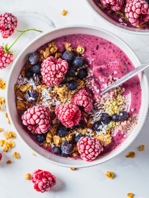 Bowl of granola topped with raspberries, blueberries and coconut shavings on a marble surface