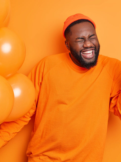 Man laughing, wearing orange and holding orange balloons