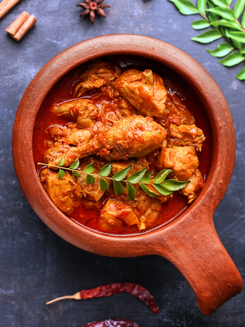 A chicken curry in a wooden pot with herbs and spices