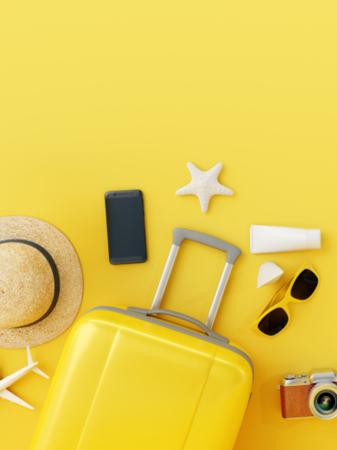 yellow background with suitcase, sunglasses, hat and holiday essentials