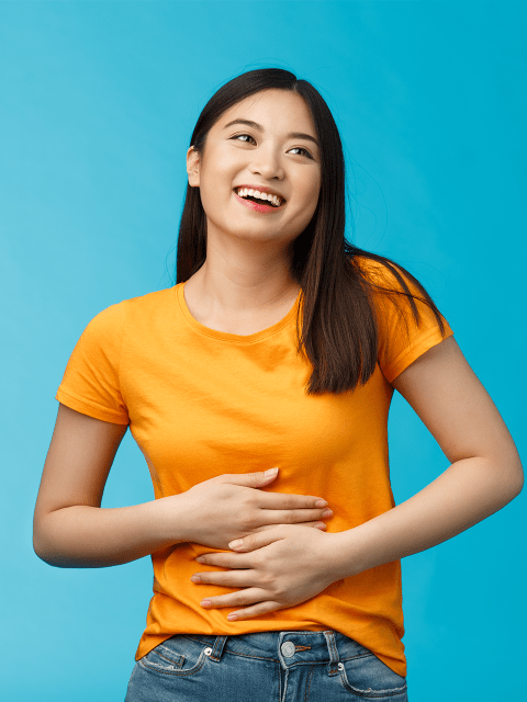 Asiatische Frau, die sich auf den Bauch greift und lacht.