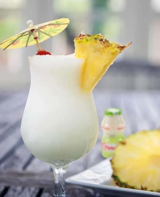 Mocktail met ananas, kokosmelk en flesje Yakult Plus met een schijfje ananas.