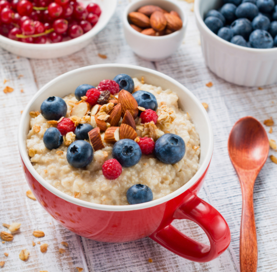 A red mug of porridge topped with almonds, raspberries and blueberries, next to a small wooden spoon