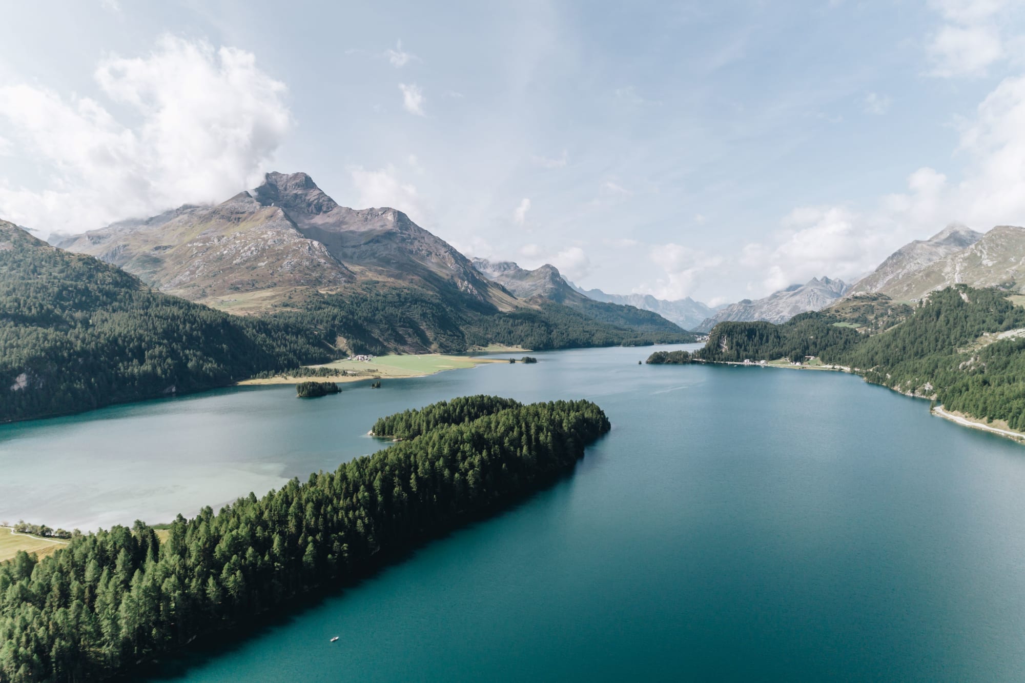 Blauer See mit Wald im Vordergrund und Bergen im Hintergrund