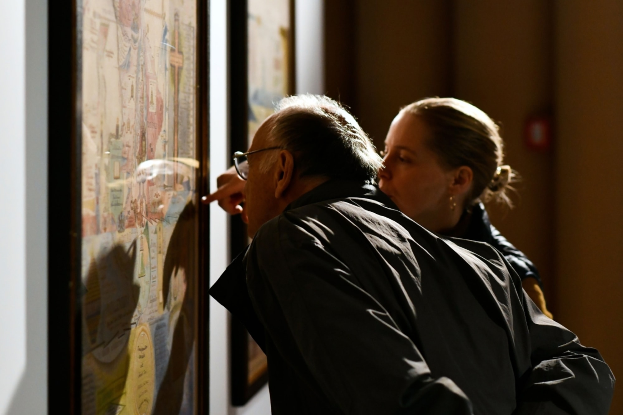 Zwei Personen betrachten in einem Museum ein gerahmtes Kunstwerk; eine Person zeigt auf ein Detail im Bild.