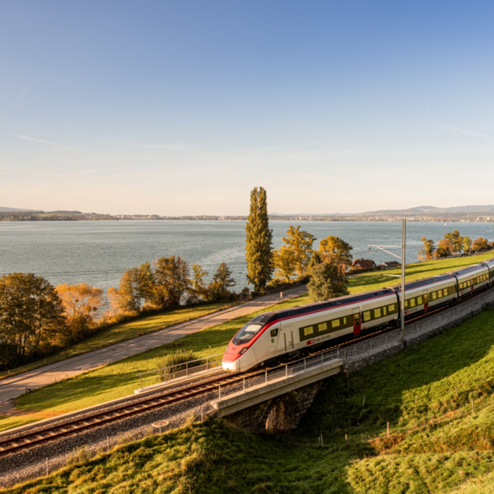 Un train traverse une prairie automnale, avec un lac en arrière-plan.