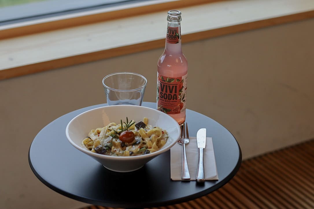 gedeckter Tisch mit Teller Pasta, Glas, Getränk und Besteck