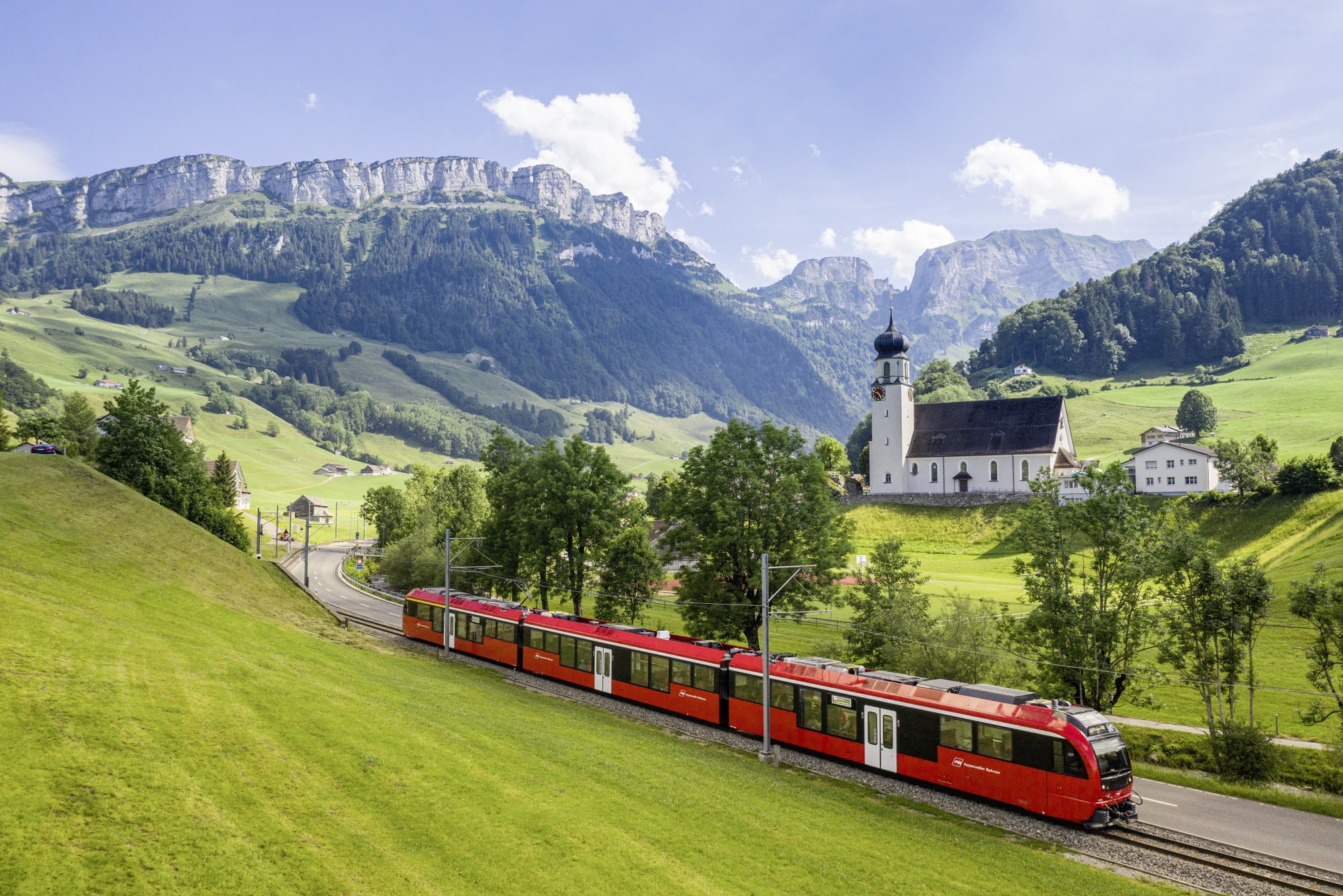 Roter Zug vor Bergkulisse und Kapelle