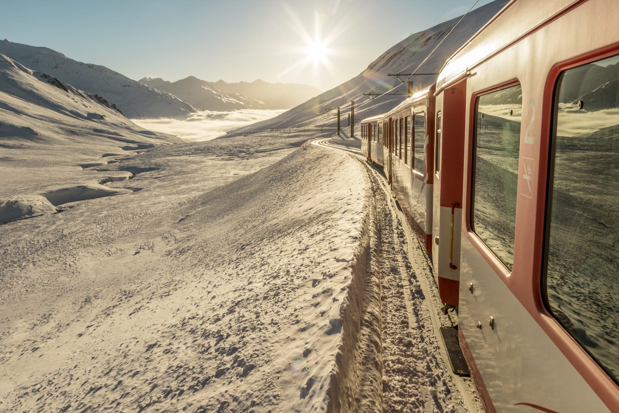 Zug fährt durch eine sonnige und verschneite Berglandschaft