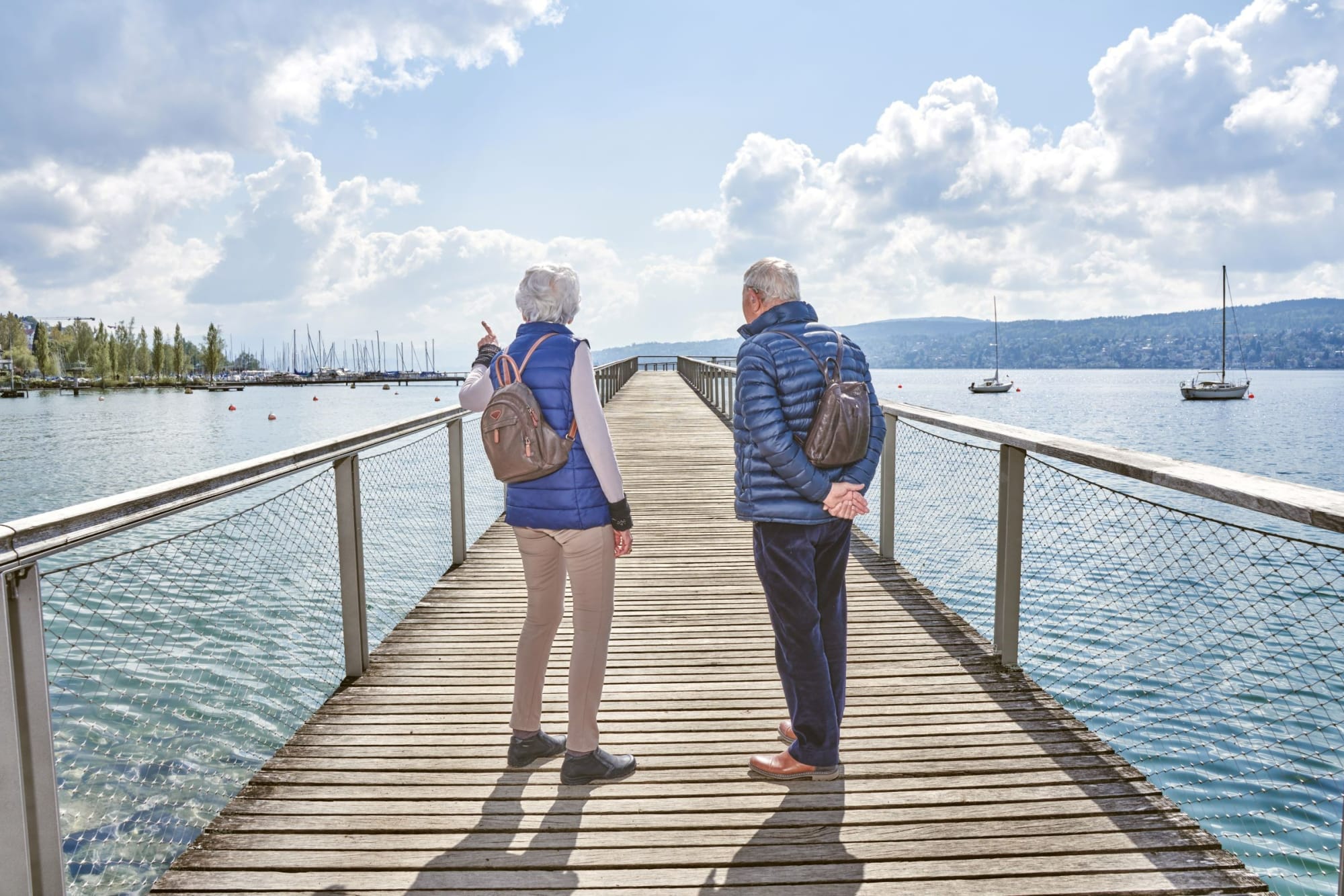 Auf dem Cassiopeiasteg über dem Zürichsee stehen ein Senior und eine Seniorin, die mit dem Finger nach links zeigt.