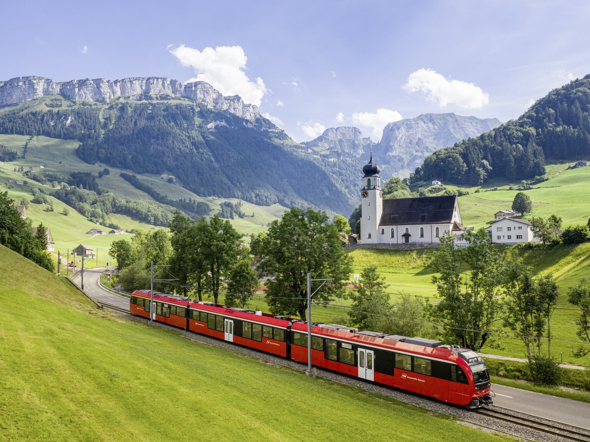 Roter Zug vor Bergkulisse und Kapelle