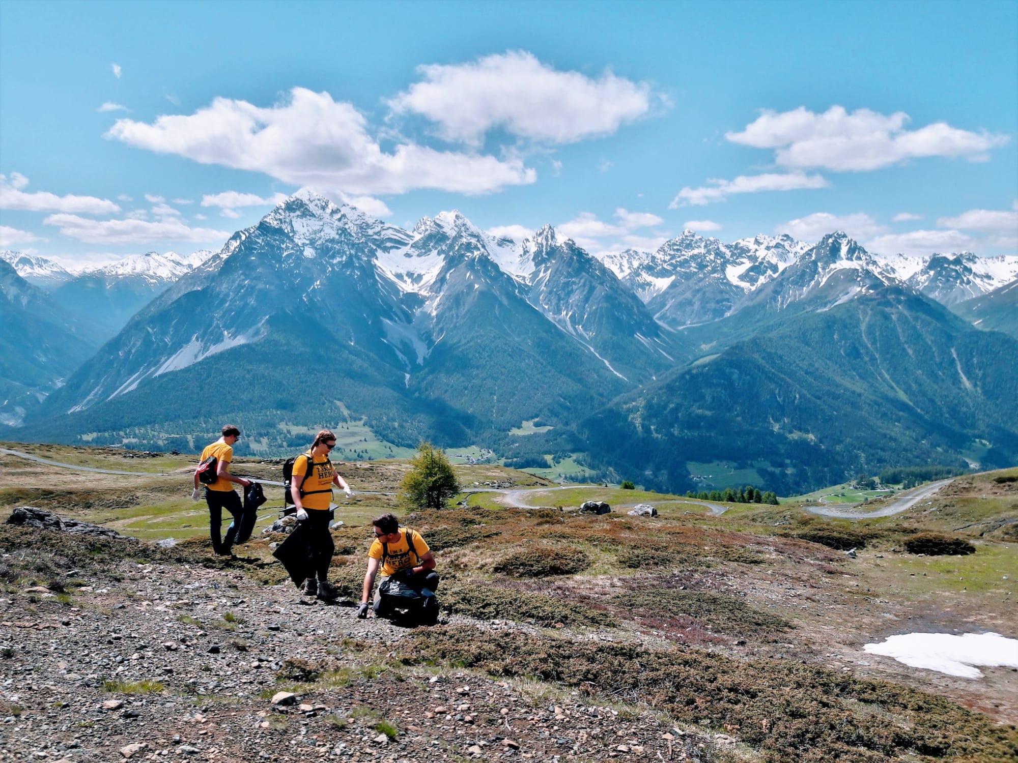 Trois personnes ramassent des déchets dans un panorama montagneux