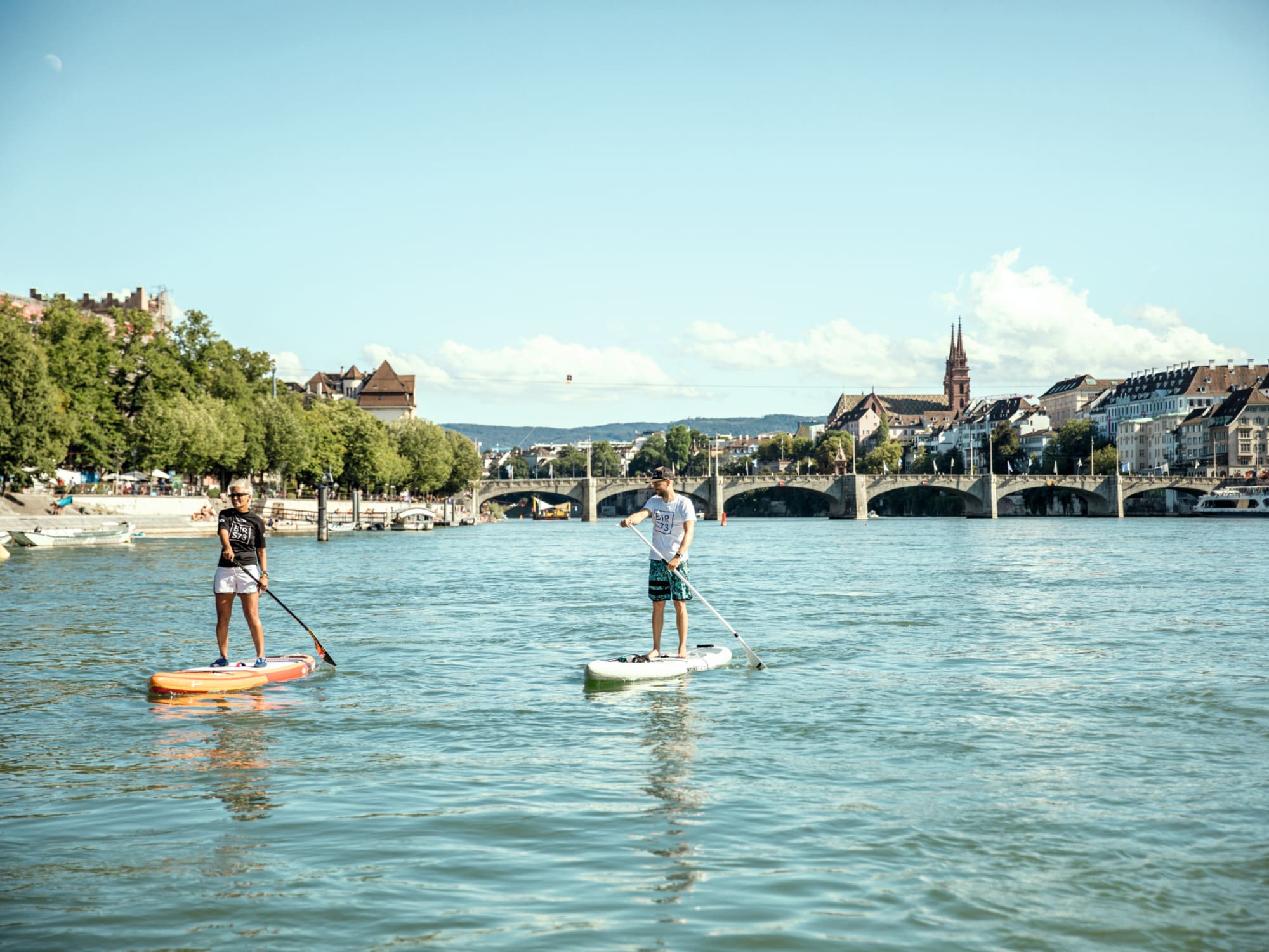 Zwei Stand-up-Paddler auf dem Rhein mitten in der Stadt Basel, Münster im Hintergrund