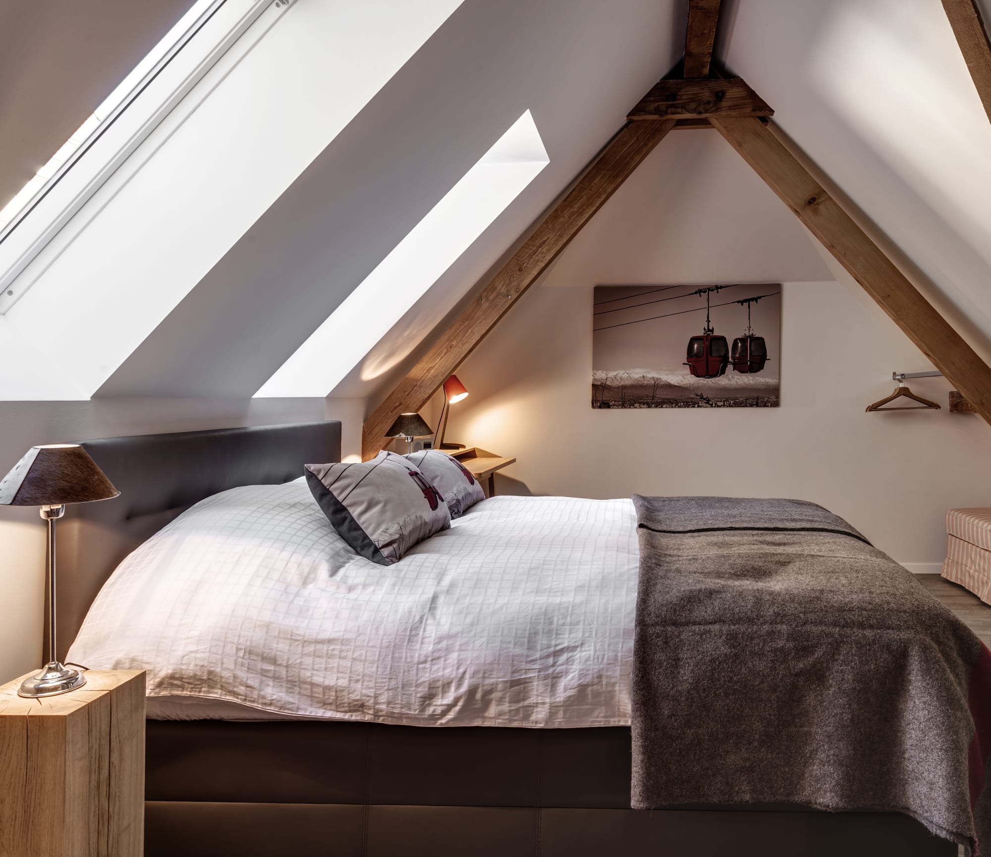 Camera degli ospiti nella luminosa mansarda con un letto a sinistra e un quadro di funivie alla parete