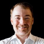 Headshot of Stas Balanevsky, smiling, in a white shirt against a black background