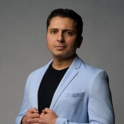 Headshot of John Mashni in a light blue blazer over a black T-shirt