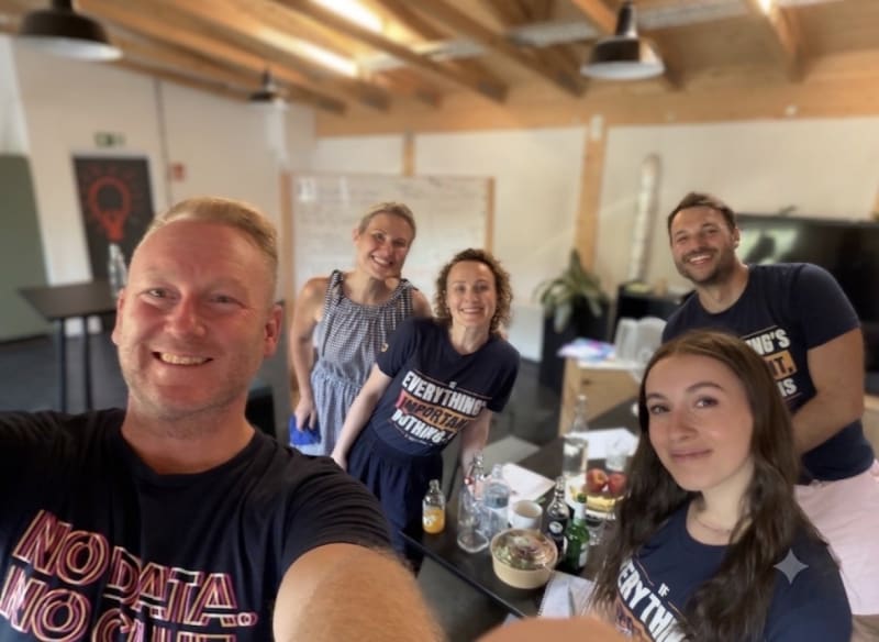 Smiling team selfie around a meeting table in a wood-beamed workshop room, ready for an EOS Quarterly meeting