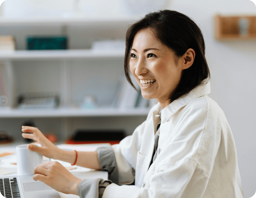 Smiling woman at her laptop holding a mug, engaged in a team conversation