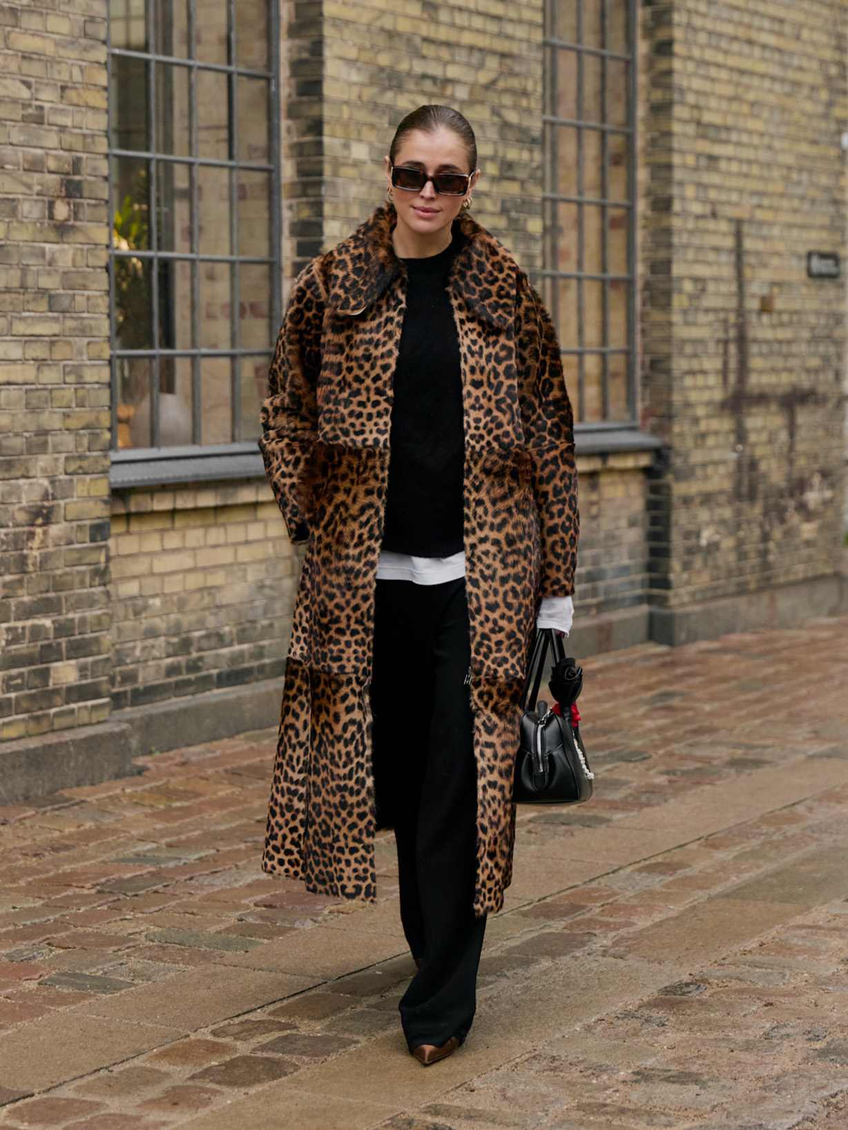 Frau trägt einen Mantel mit Leo-Muster zu einer schwarzen Hose und schwarzen Stiefeln 