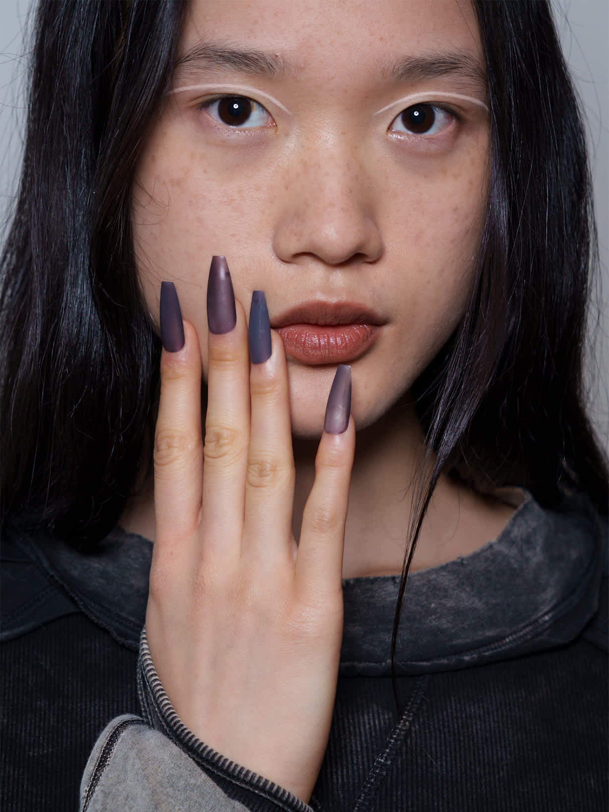 Czarnowłosa kobieta prezentuje manicure w modnym kolorze smokey amethyst