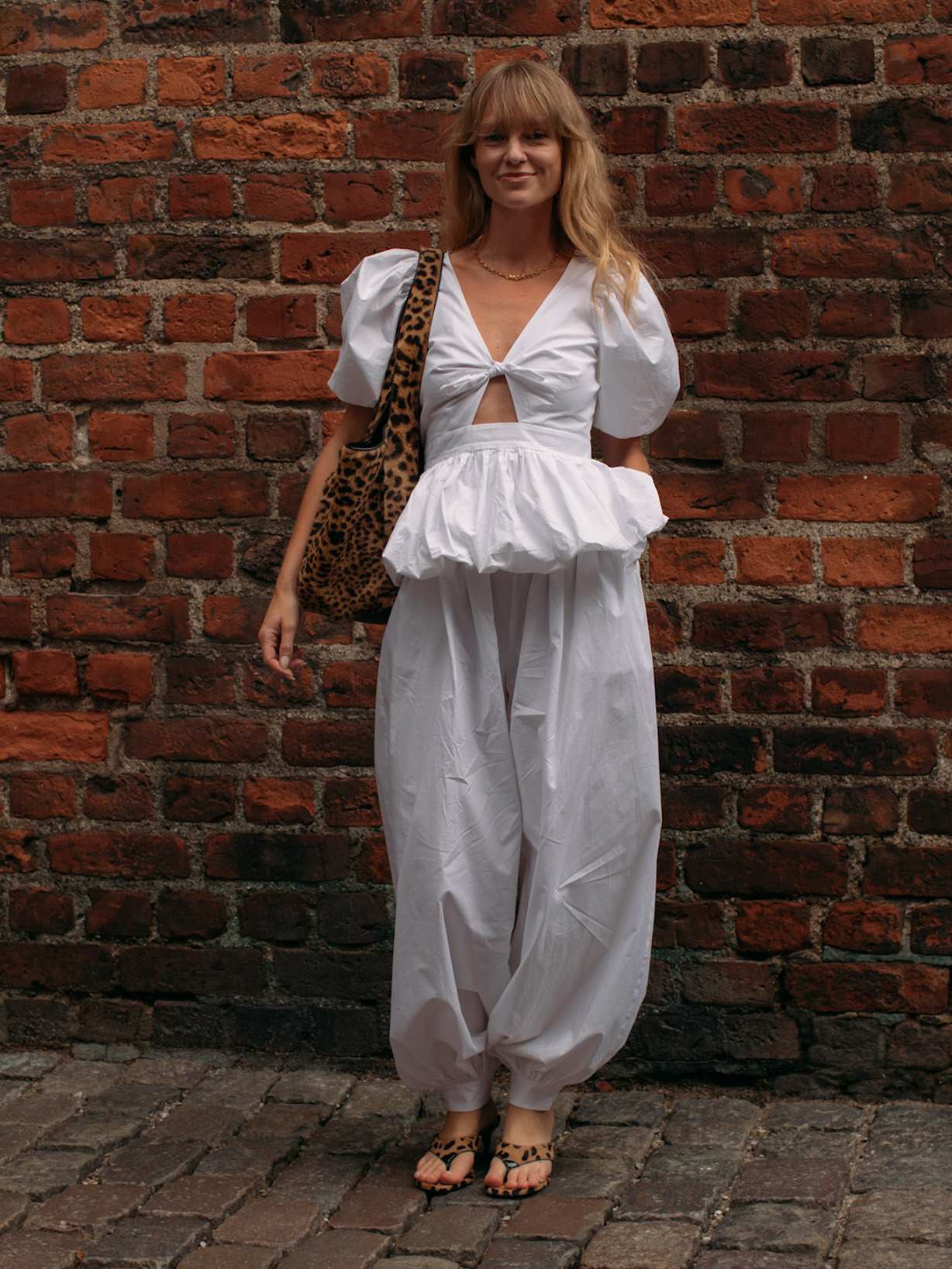 Jeanette Madsen trägt eine weiße Bluse und eine passende Ballonhose, dazu einen Shopper mit Leo-Muster. 