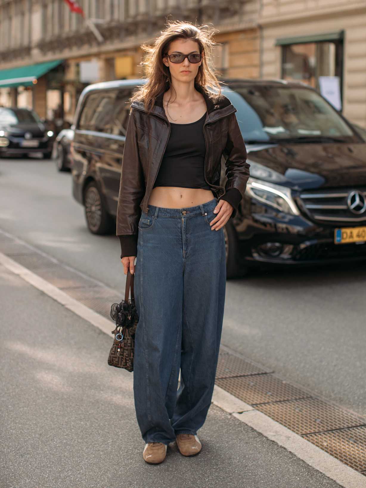 Kobieta w jasnobrązowych sneakersach Puma Speedcat z zamszu, jeansach i brązowej skórzanej kurtce