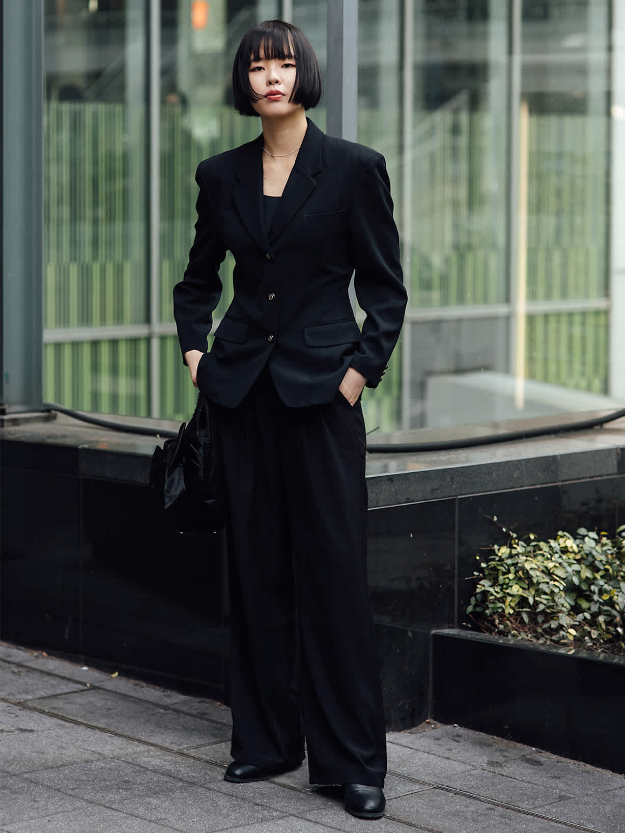 Frau in schwarzem taillierten Blazer und weiter Hose vor einer modernen Glasfassade