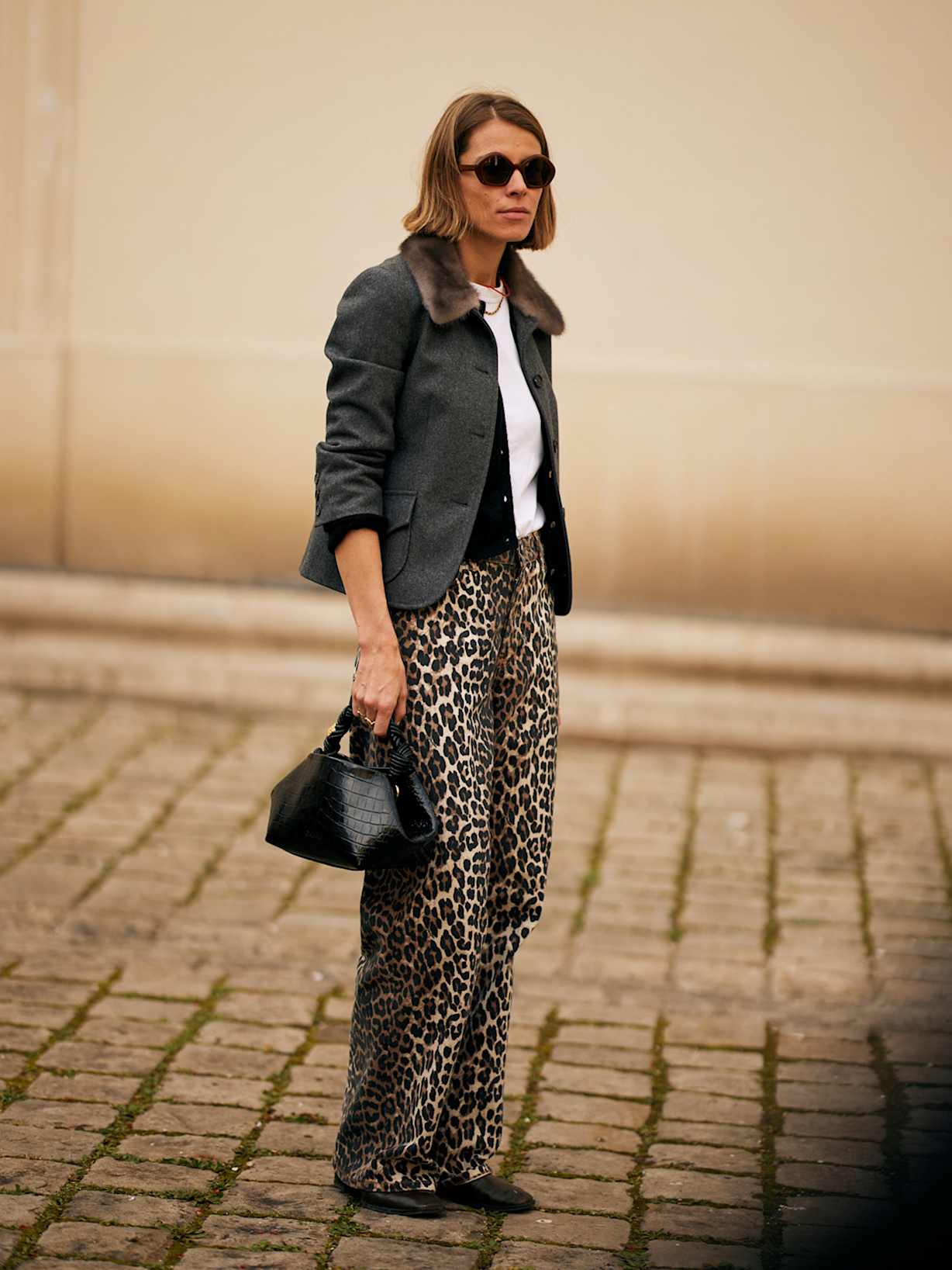 Frau trägt eine Hose mit Leo-Muster zu weißem T-Shirt und einem grauen Blazer. 