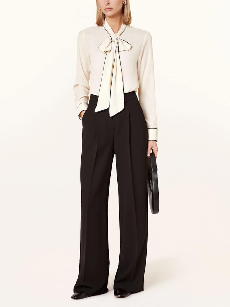 Blonde Frau trägt cremefarbene Schluppenbluse mit schwarzer Stoffhose