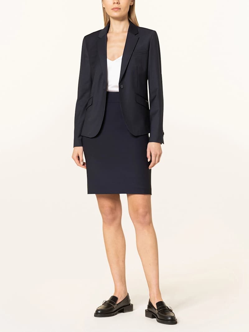 Blonde Frau trägt Business-Kombination aus schwarzem Rock, Blazer und weißer Bluse