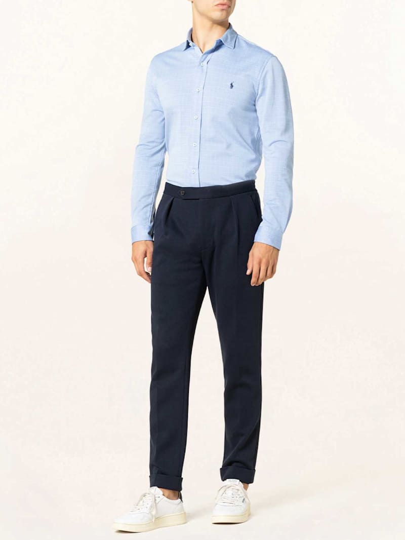 Mann trägt ein hellblaues Hemd zu einer dunkelnlauen Chino und hellen Sneakers