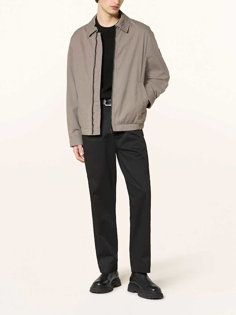 Mann trägt ein schwarzes Outfit und einen grauen Blouson