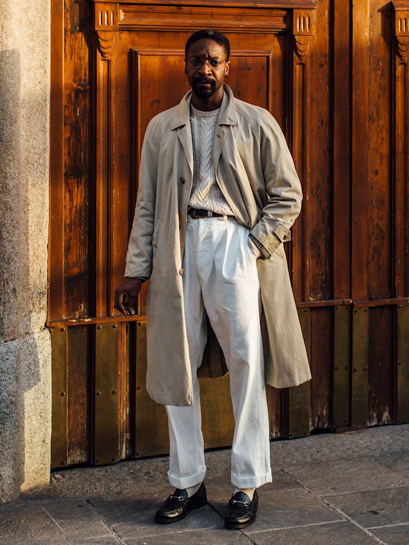 Mann trägt einen klassischen Trenchcoat zu einer weißen Hose und zum Strickpullover