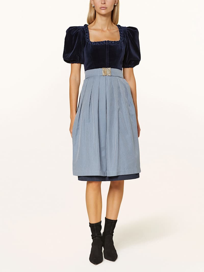 Blonde Frau trägt dunkelblaues Dirndl mit Balkonettausschnitt und hellblauer Schürze