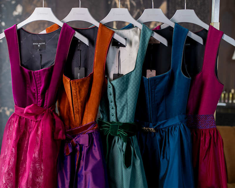 Fünf Dirndlkleider in verschiedenen Farben hängen auf Bügeln an einer Kleiderstange