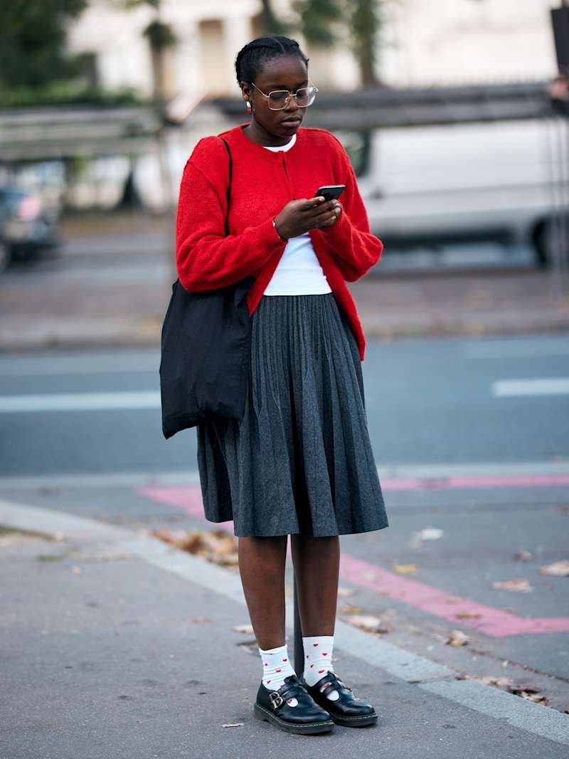Frau trägt einen roten Cardigan zu einem grauen Faltenrock
